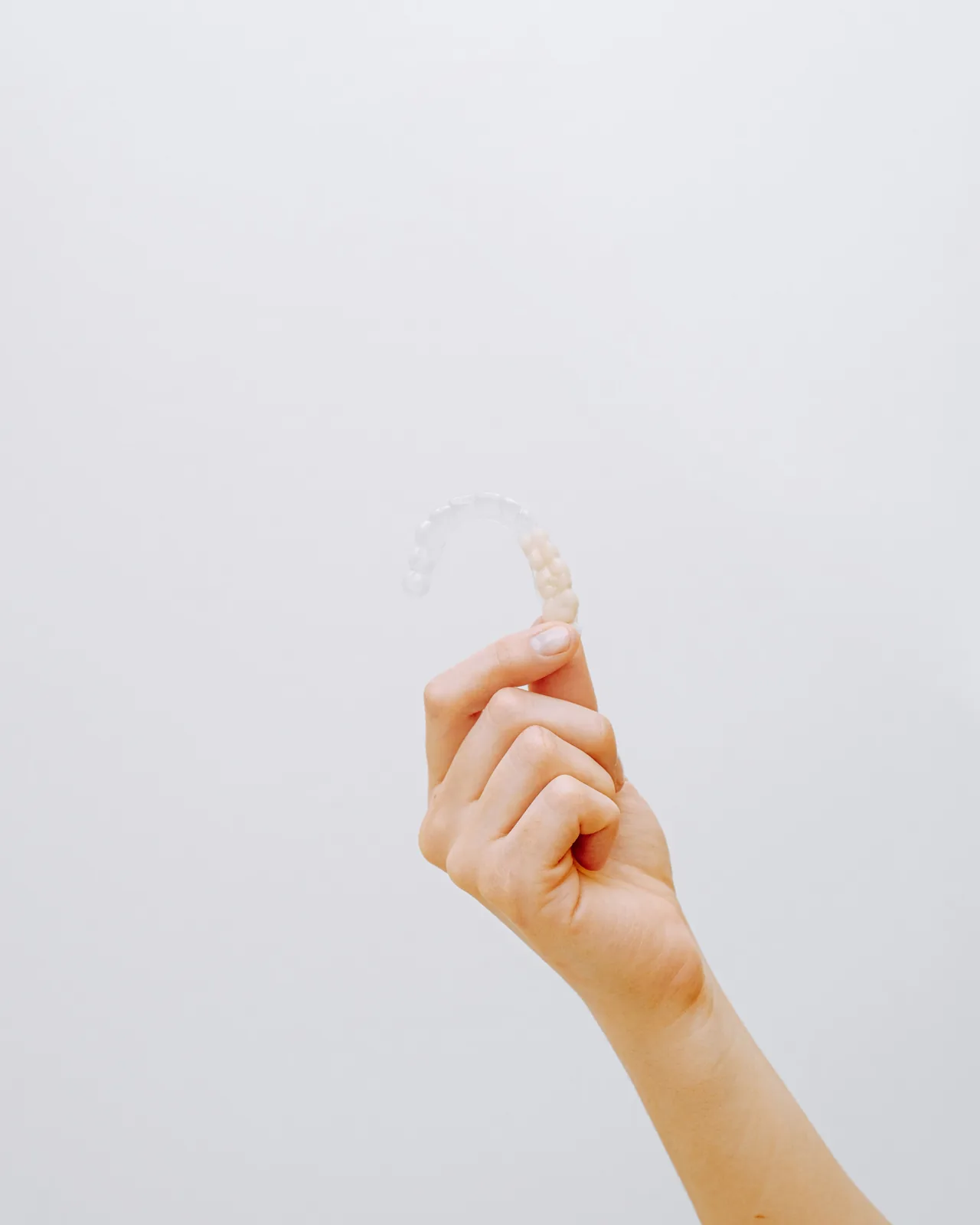 A hand holds a transparent dental aligner against a clean white background.