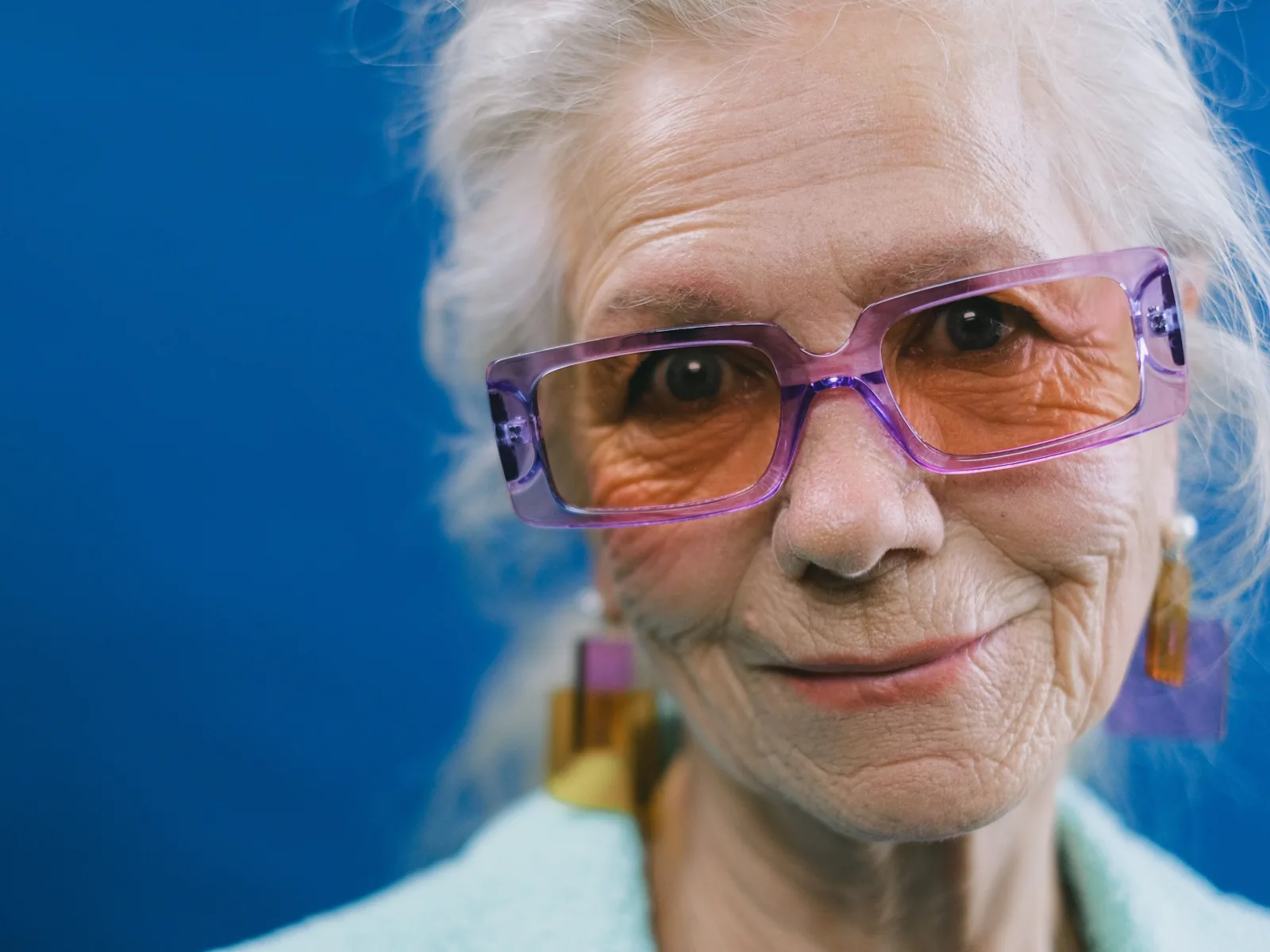 An older woman with gray hair and purple glasses smiles at the camera.