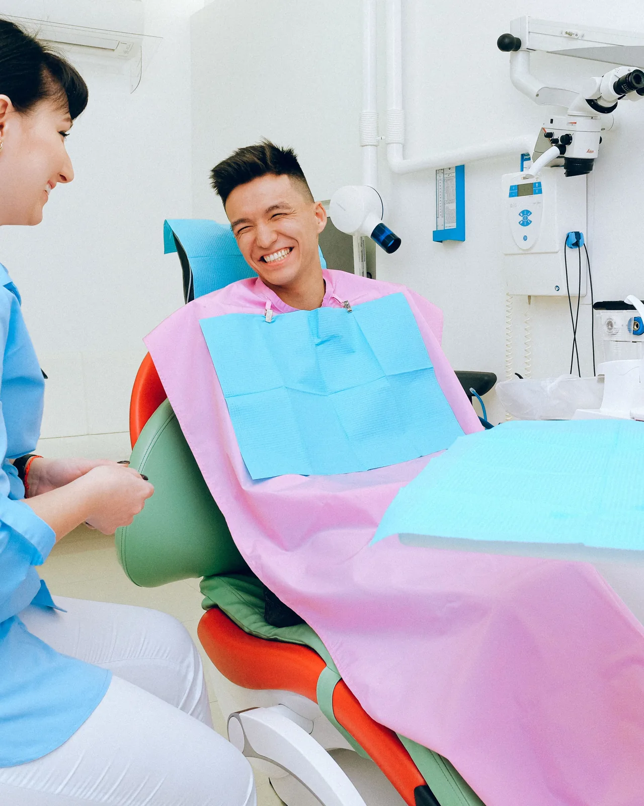 A smiling man speaks with a dentist beside a dental chair in a bright clinic.