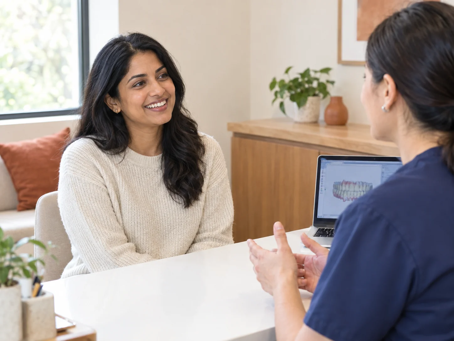 A friendly dental team member greets a smiling teen patient at a warm modern reception counter.