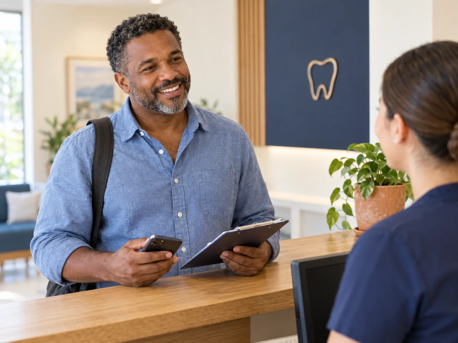 A smiling patient chats with a receptionist at a bright modern dental clinic reception counter.