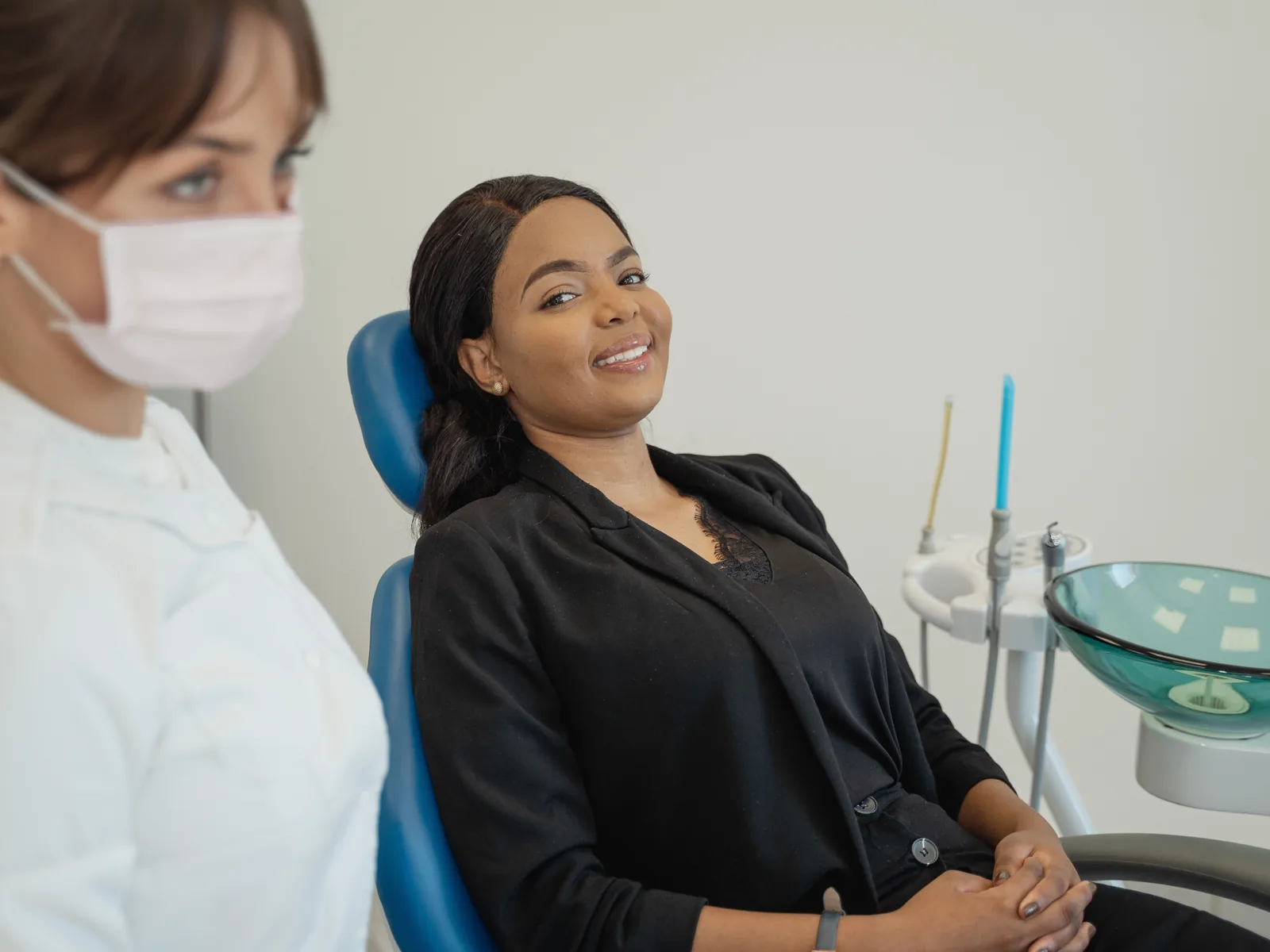 A smiling woman sits comfortably in a dental chair while a clinician stands nearby.