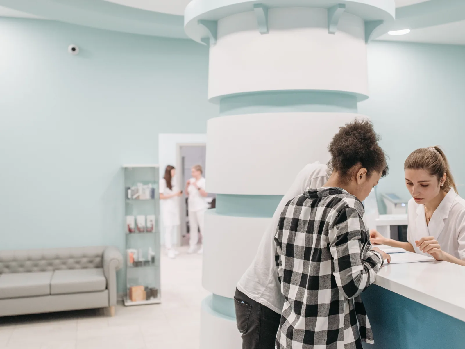 A patient reviews paperwork with a receptionist at a bright clinic desk.