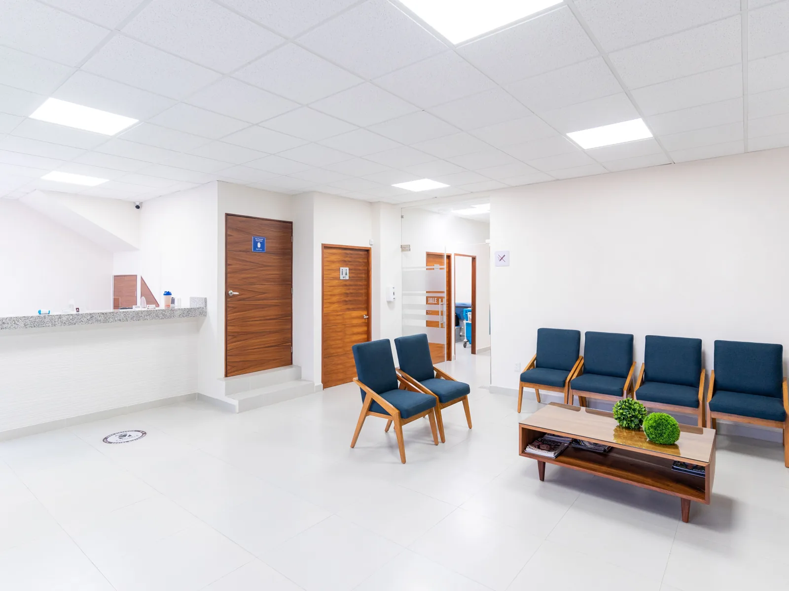 An empty, bright clinic waiting room with blue chairs and a reception counter.